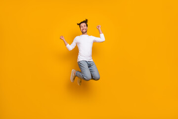 Fototapeta na wymiar Full length photo of cool brunet young guy jump hands fists wear shirt jeans footwear isolated on yellow background