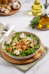 Arugula salad with shrimp and champignons, olive oil and dill on a wooden board on a white surface