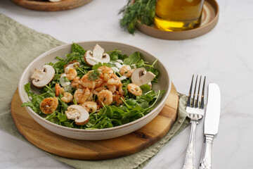 Arugula salad with shrimp and champignons, olive oil and dill on a wooden board on a white surface