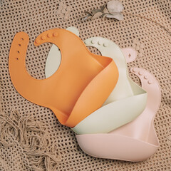 Fototapeta premium Three silicone baby bibs of different colors on beige blanket. Flat lay. Square frame instagram use