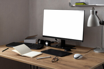 White blank screen monitor on the wooden table,tablet for drawing and designing,opened notebook and pen,mouse,lamp against white wall.Empty space