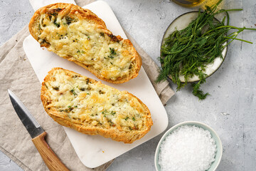 Two halves of garlic and butter bread - baguette on a marble board, sea salt, pepper, dill and garlic cloves on a grey concrete background, top view