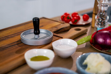 Obraz na płótnie Canvas Burger press on wooden cutting board, vegetables and spices with kitchen bowls.