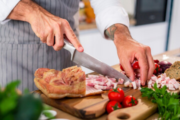 The cook is cutting bacon on a wooden board in kitchen