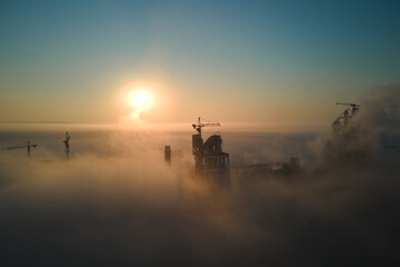 Aerial view of cement factory with high concrete plant structure and tower crane at industrial production site on foggy morning. Manufacture and global industry concept