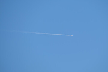 Distant passenger jet plane flying on high altitude on clear blue sky leaving white smoke trace of contrail behind. Air transportation concept