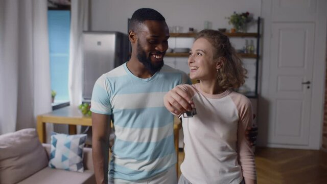 Happy diverse couple hugging and showing new home keys at camera. Realtime