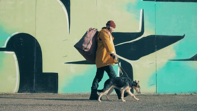 A tramp is walking along the street with a dog and a massive bag
