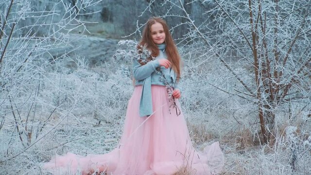 Charming beautiful cute little girl fantasy princess in winter snowy park, holds snow covered branch in hands. Smiling happy face. Pink lush long dress. Child fashion model. fabolous nature tree frost