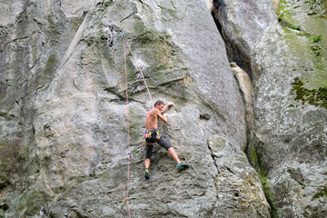 Young man climbing steep wall of rocky mountain. Male climber overcomes challenging route. Engaging in extreme sport concept