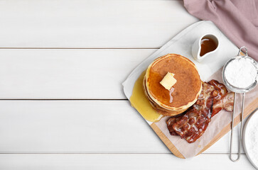 Delicious pancakes with maple syrup, butter and fried bacon on white wooden table, flat lay. Space for text