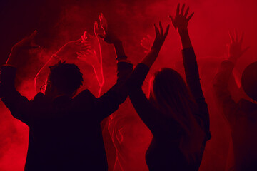 Dark silhouettes of young people dancing and raising hands while enjoying party in smoky nightclub...