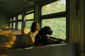 Obraz na płótnie Canvas a European woman in sunglasses and a Labrador retriever dog in an empty train car are driving and looking out the window. traveling with a dog on public transport in the city or to nature. a romantic