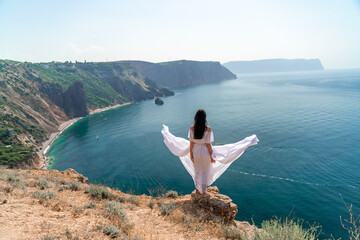 Portrait of a young woman on the beach by the sea, sitting with raised hands in a white dress and hat. Back photo