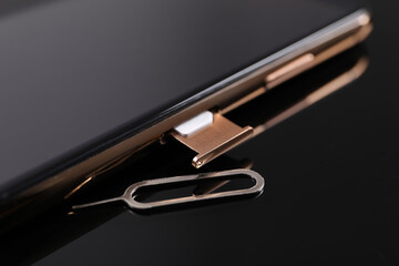 SIM card, smartphone and ejector on black background, closeup