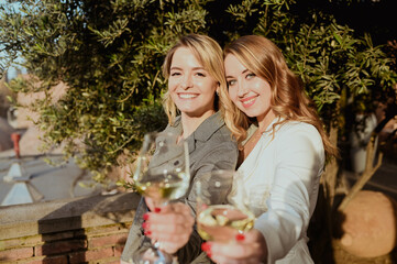 Close-up portrait of two female friends in strict suits laughing drinking wine on the terrace...