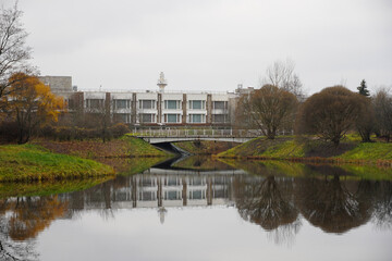 Modern building in old autumn park near pond with mirror water. Grey sky . Babolovsky park in...