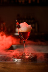 Close-up of wine glass with foamy cocktail decorated with red berry and small heart on the bar