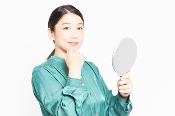 白い背景の前に立って、鏡で肌のチェックをする主婦