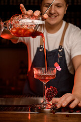 hand of bartender holds mixing cup with cocktail and gently pours it into wineglass