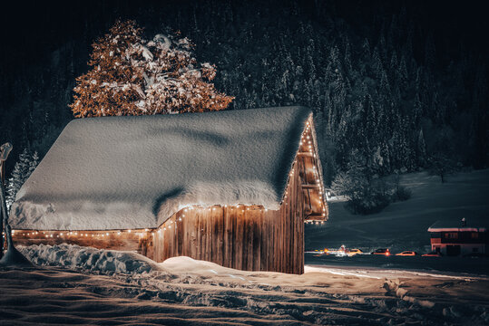 Night photography of a wooden cottage covered by snow. Snowy mountain landscape. Malborghetto Valbruna, Udine province, Friuli Venezia Giulia, Italy