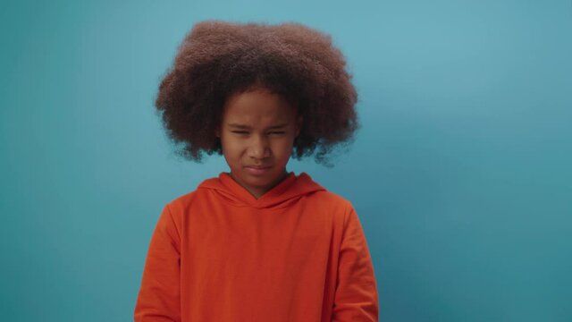 African American girl shows angry emotion standing on blue background. Kid disagrees with something.
