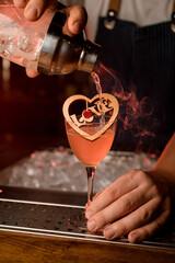 Close-up of male hand holding wineglass with wooden decoration and pours a steaming cocktail from shaker