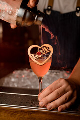 Close-up of male hand holding wineglass with wooden decoration and pours a steaming beverage from shaker