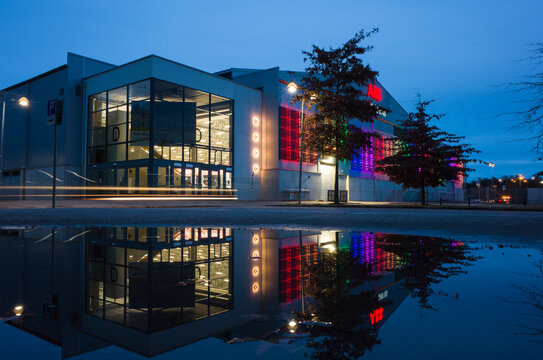 Vasteras, Sweden - 18 October, 2021: Building of ABB Arena at Rocklunda reflected in puddle on parking lot at dusk, Scandinavian sport arena facade in evening