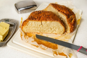 Sliced homemade bread on cutting board, knife, butter.