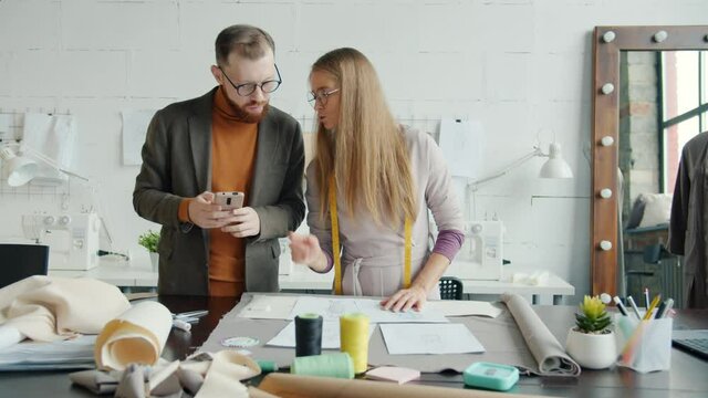 Girl and guy creative designers are working in studio checking sketches and using smartphone. Professionals and modern technology concept.
