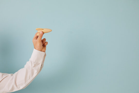 Human Hand Holding Wooden Rocket On Blue Color Blank Copyspace Background As Metaphor For Implementing Innovation And Launching New Business That's Ready For Challenge, Moving Forward And Developing