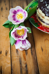 homemade chocolate cake and spring flowers on wooden table close up