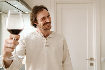 Ginger bristle man smiling and winking while drinking wine in kitchen