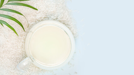 Rice milk. Vegan eco friendly food composition with glass cup of plant rice milk with rice seeds and palm leaf on a blue background with copy space. Dairy free, non lactose product