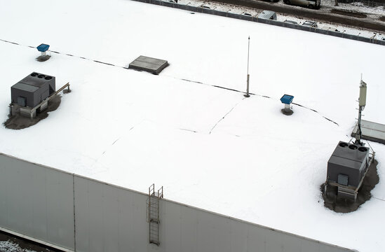 Roof of a commercial building with a external units of the commercial air conditioning and ventilation systems, cellular antenna and lightning rod. Winter photo..