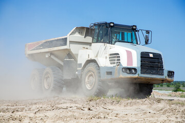 Large articulated dump truck with a white cab at a construction site during excavation work against blue sky. loading and transportation of soil . Dusty road