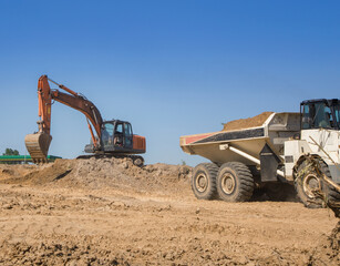 orange crawler excavator and articulated dump truck during the excavation stage at a construction...