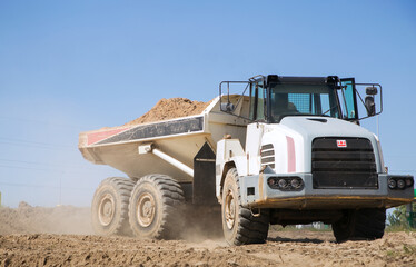 large gray articulated dumper at a construction site drives down a dusty road . loading and transportation of soil.