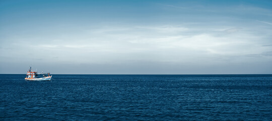 A fishing boat floats alone in the calm sea. The sky background above the horizon for copy space....