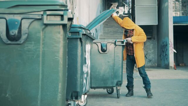 A tramp is rummaging in the trash bins