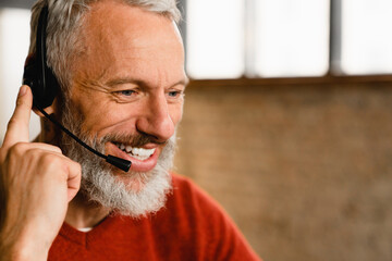 Closeup portrait of a IT support customer support manager. Mature middle-aged man freelancer in headset listening to the client on hotline, having video call online