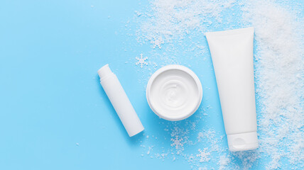 Facial cream containers mockup with snow top view, copy space, winter skin care, skin nourishing and moisturizing, blue background