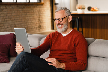 Videocall conference meeting online. Caucasian middle-aged mature man in glasses talking on digital tablet with colleagues, friends, relatives on social media applications at home