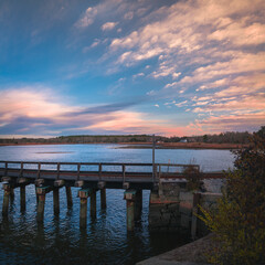Fototapeta premium Beautiful sunrise seascape with the view of old railroad bridge and dramatic clouds along coastal village in Wareham, Massachusetts. Travel landscape theme for New England, train, trip, or nostalgia.