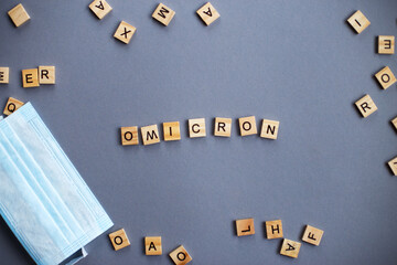 word omicron made by wooden blocks with medical mask on gray background.