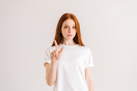Portrait of confident young woman shaking finger in prohibition gesture, show no and disagreement, standing on white isolated background in studio. Serious redhead female shaking head in disagreement