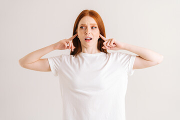 Portrait of displeased young woman covering her ears and gesticulating say no bla-bla-bla standing on white isolated background in studio. Irritated redhead female showing nonsense content.