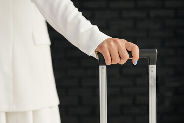 Woman in a white dress standing next to a suitcase holding its handle