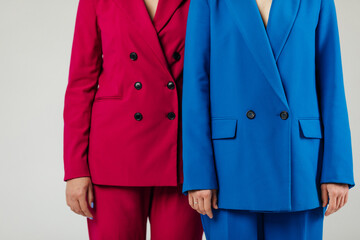 Two young happy female models in blue and red suits in front of the white wall